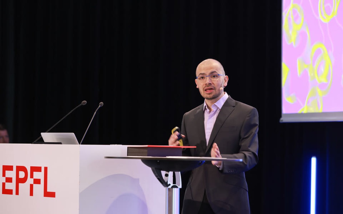 Demis Hassabis speaking at a lectern during an EPFL event
